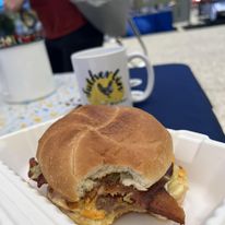 Bacon cheese burger with bite out next to Sutherlin Farmers Market mug