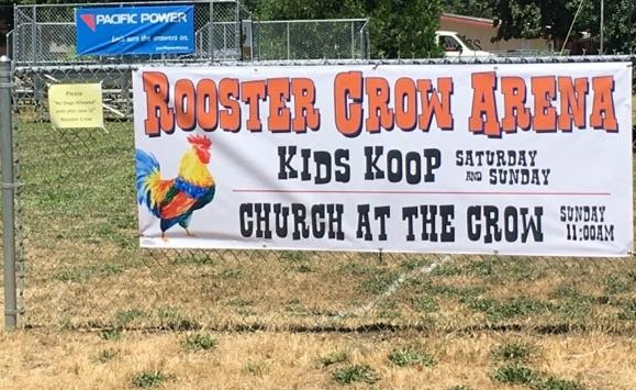 Banner hung on chain link fence with lettering for Rooster Crow Arena.