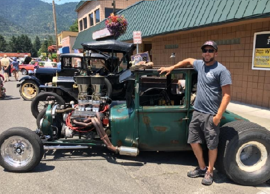Man posing in front of a hot rod.