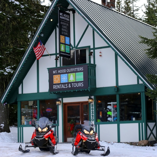 front of Mt Hood Outfitters building covered in snow with snowmobiles parked out front.