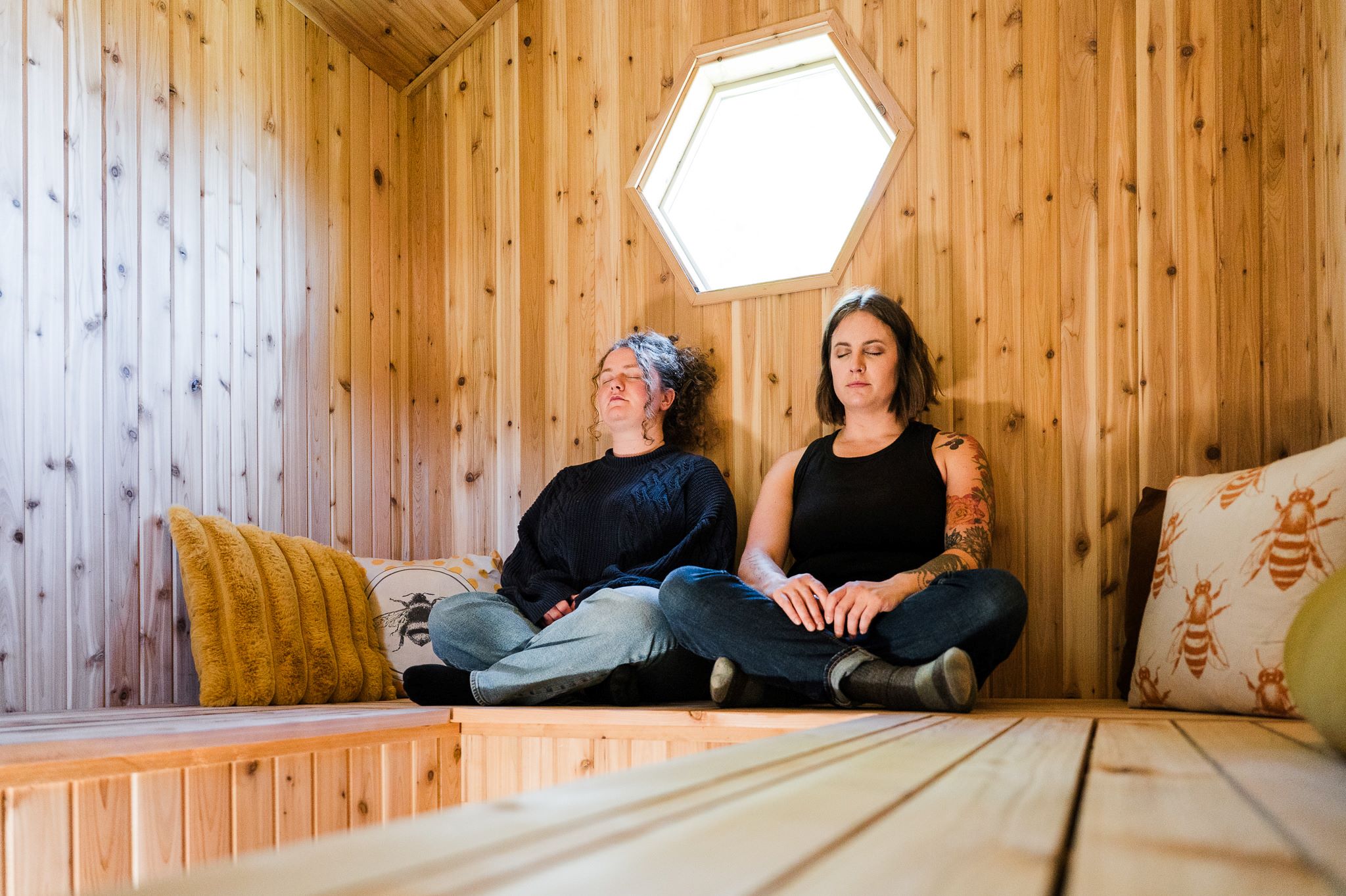 two women wearing black clothes sit cross legged inside a cedar room