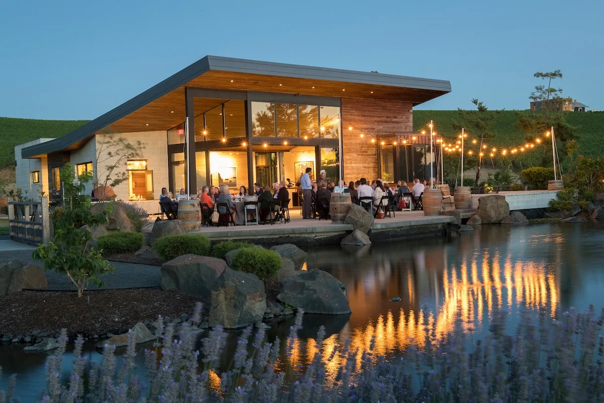 Exterior of wine tasting room at dusk with twinkle lights and people sitting on the outdoor patio