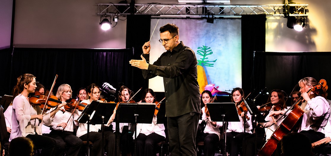 A group of musicians play various instruments with a conductor holding a baton