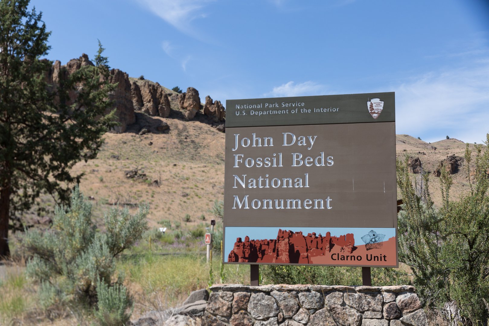 national monument park sign in foreground with rocky hills and sagebrush in background