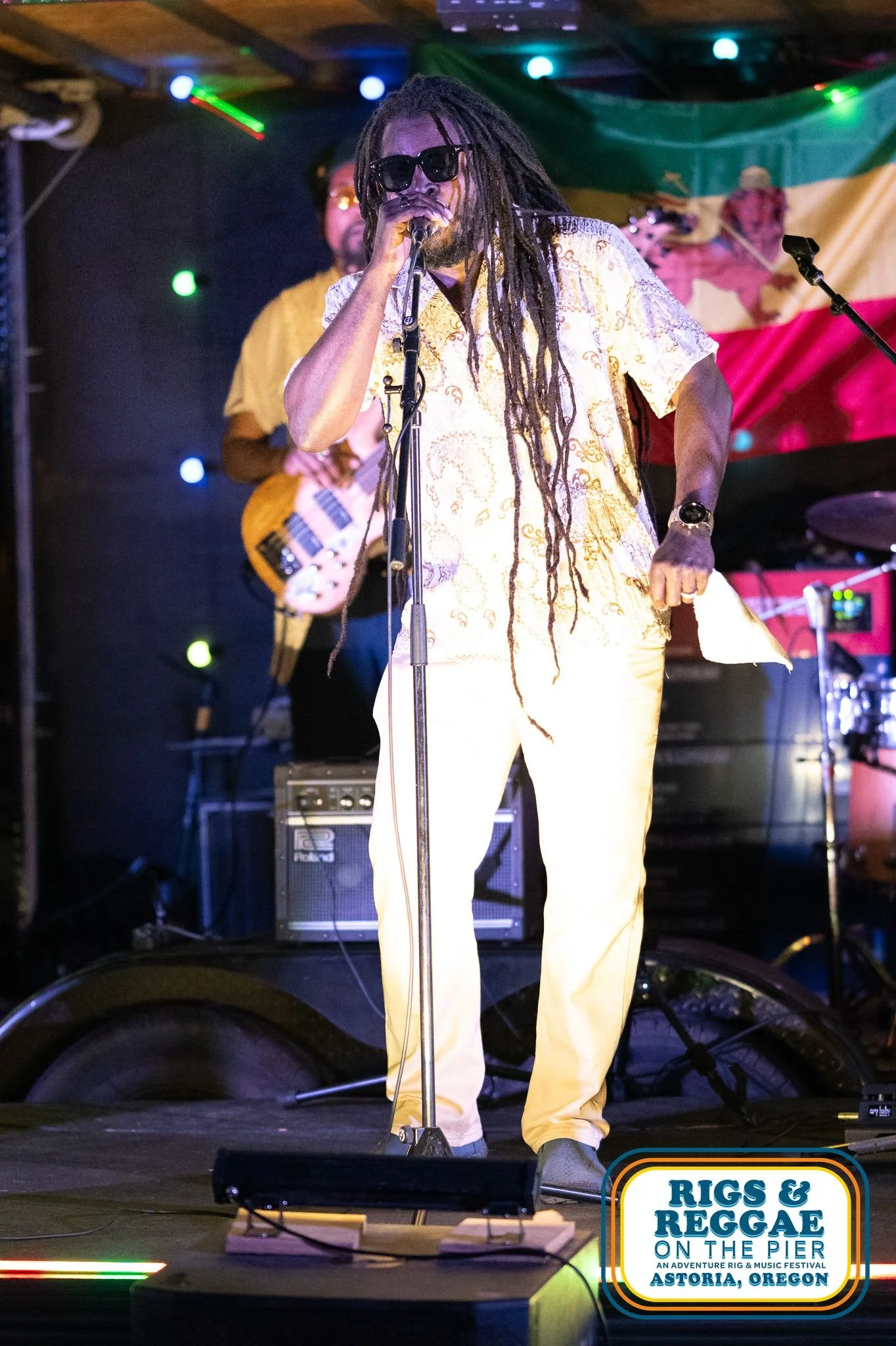 Reggae musician with waist length dreadlocks wearing pale yellow clothes and sunglassesperforms on stage