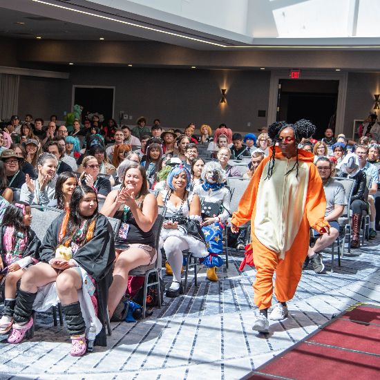 People sitting in chairs watching a runway show with a person in costume