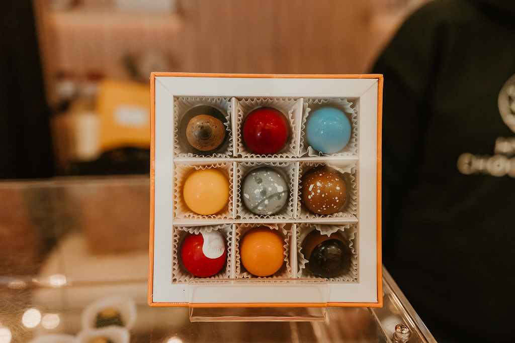 A display of nine round colorful chocolate truffles in a yellow box