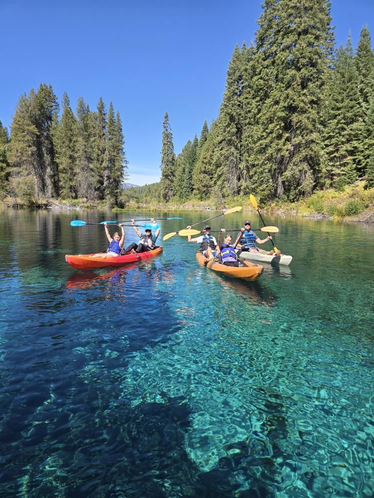people in kaykas holding oars in the air smiling while floating on clear blue water