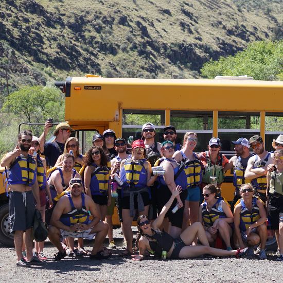 group of people smiling in life jackets in front of a yellow school bus