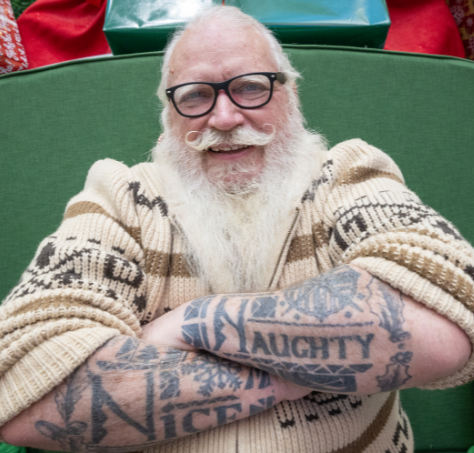 Hipster Santa dressed in sweater with black rimed glasses and tattoos