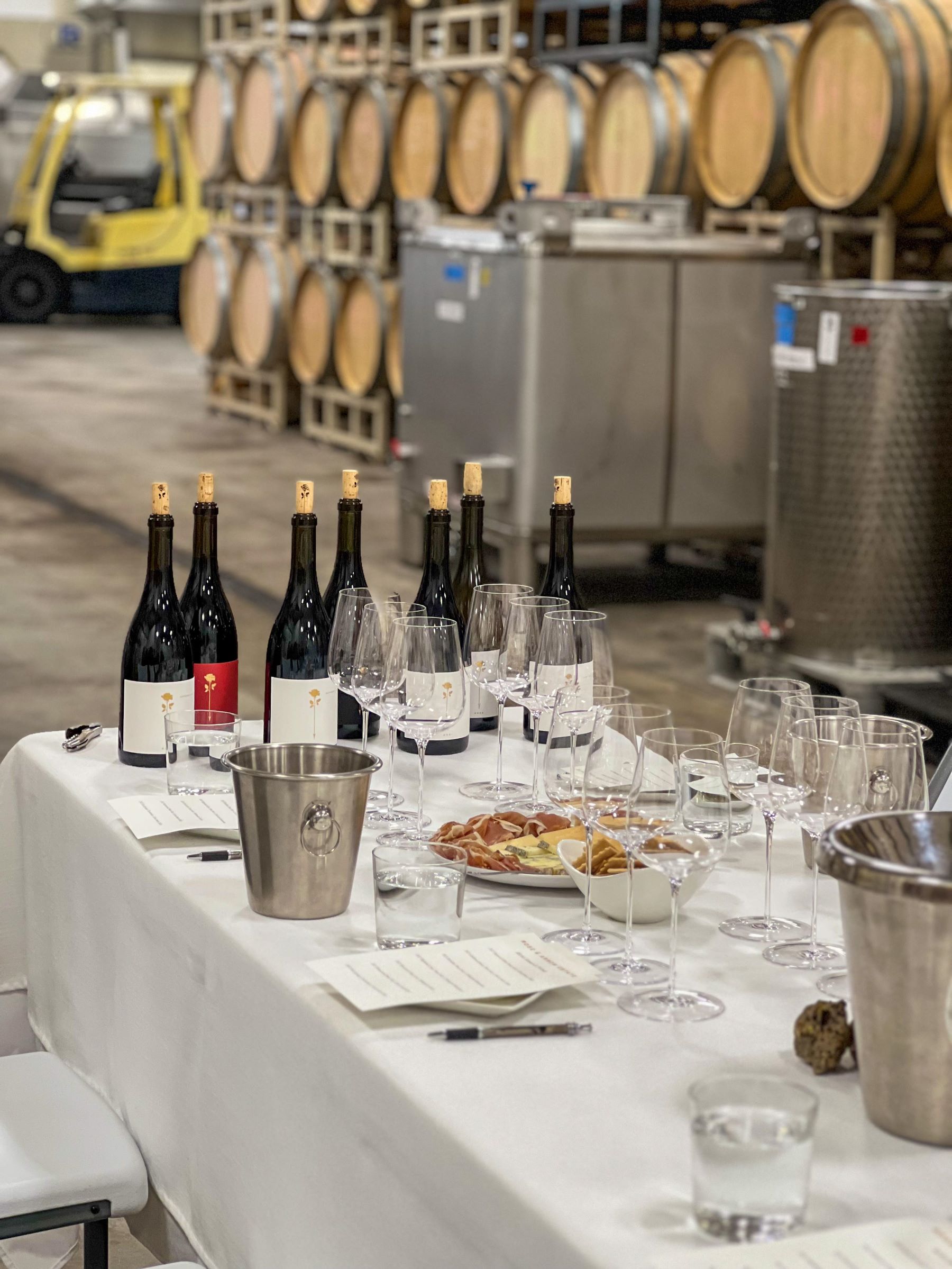 Interior of a winery barrel room with a table dressed with wine glasses and bottles and a charcuterie board for a wine tasting