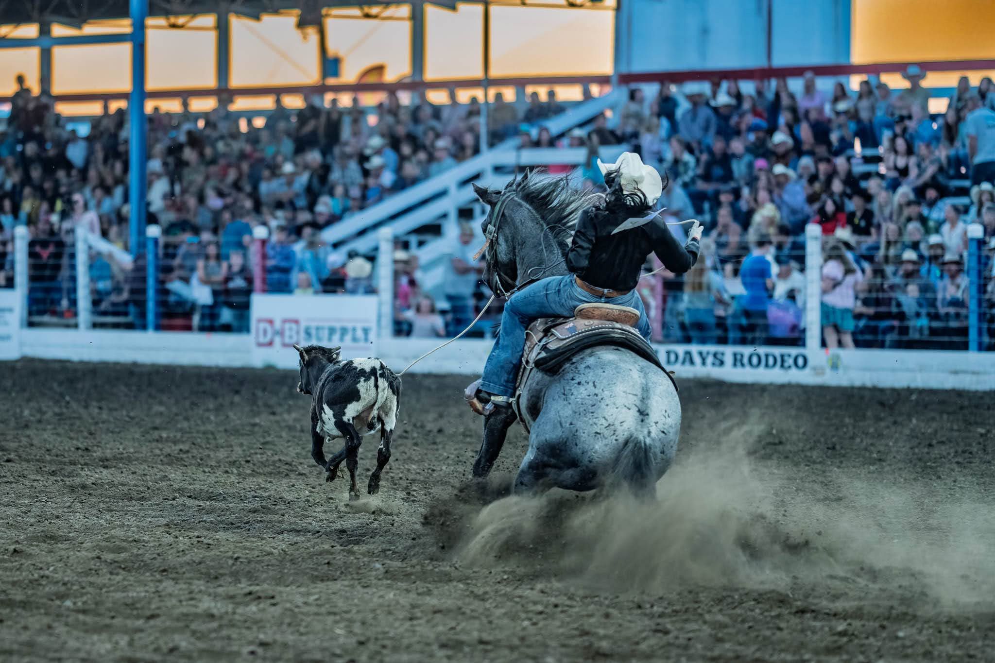 A cowgirl wearing a white cowboy hat rides a horse in a rodeo arena