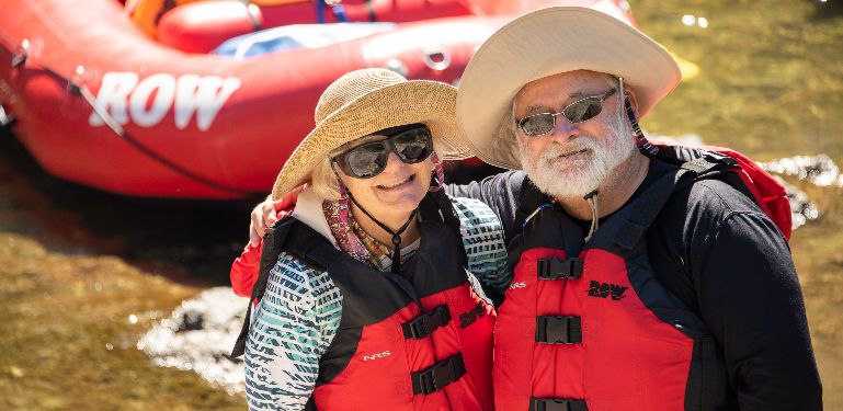 couple smiling in front of river raft  wearing life jackets