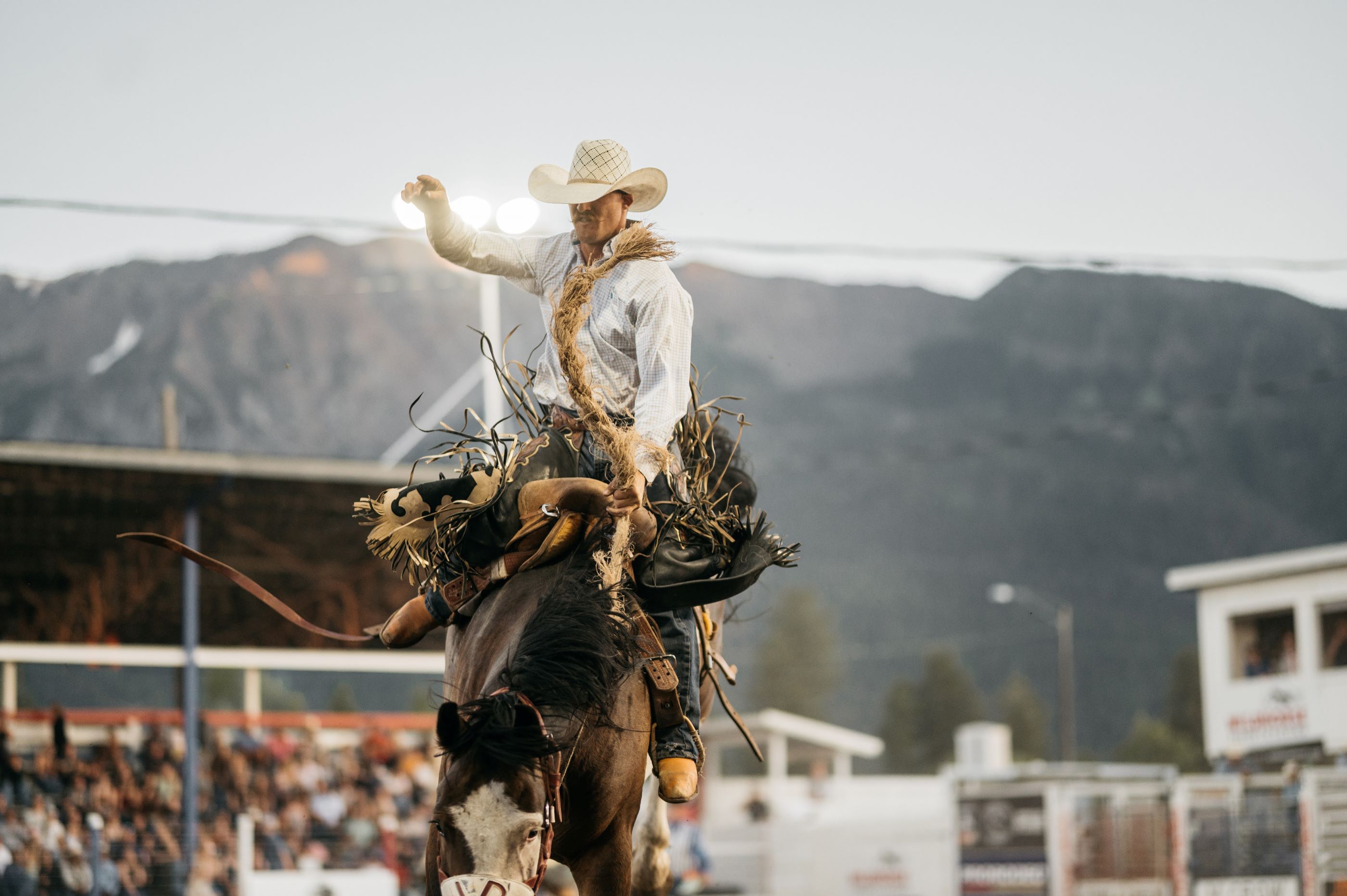 A cowboy in a white cowboy hat riding a bucking bronco in front of a crowd at a rodeo
