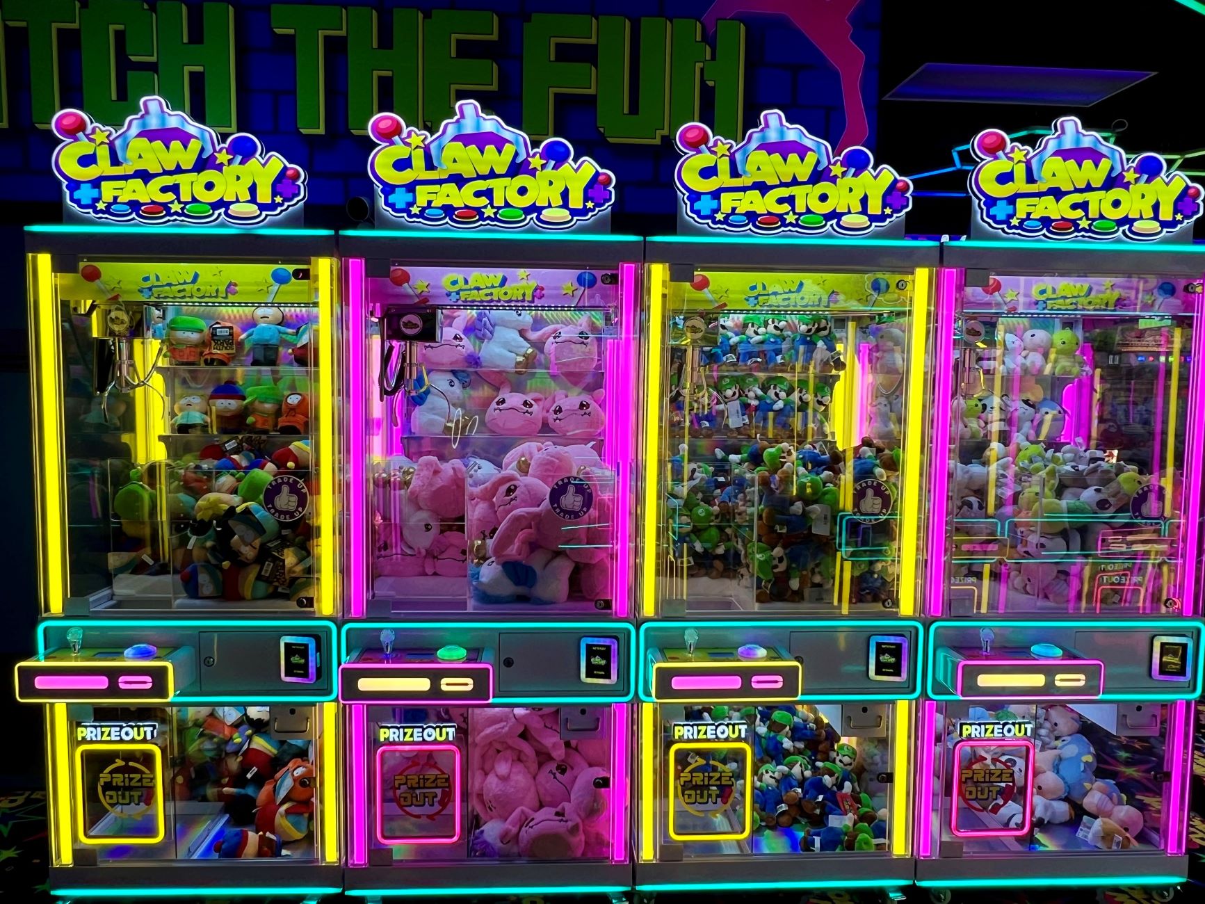 Four claw factory arcade games in a row full of colorful stuffies and toys