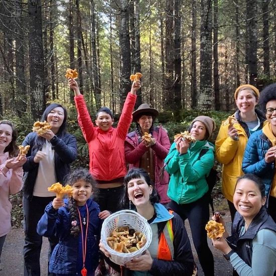 group of people in the forest holding wild foraged mushrooms