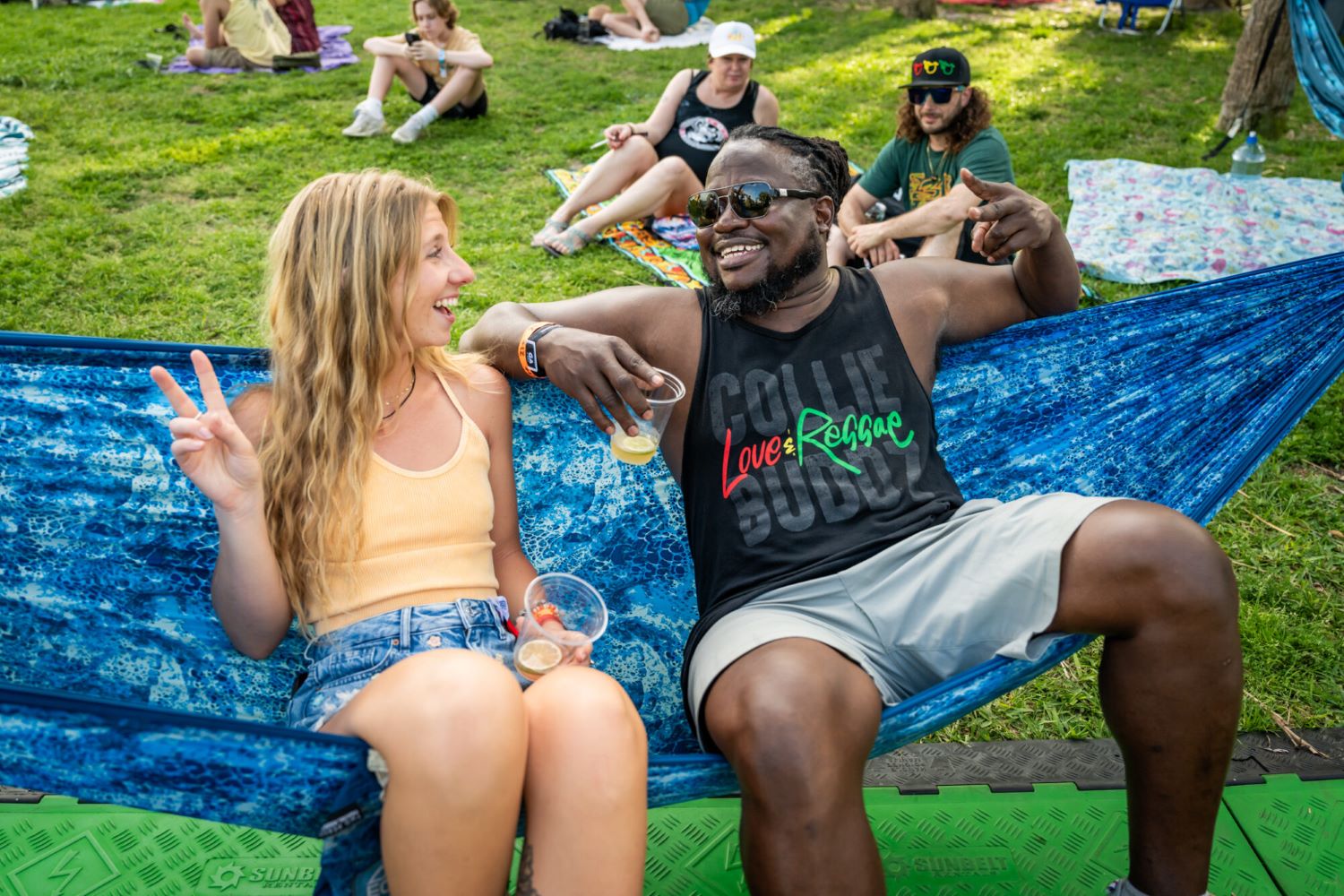 two people sitting on a colorful hammock smiling and holding up the peace sign