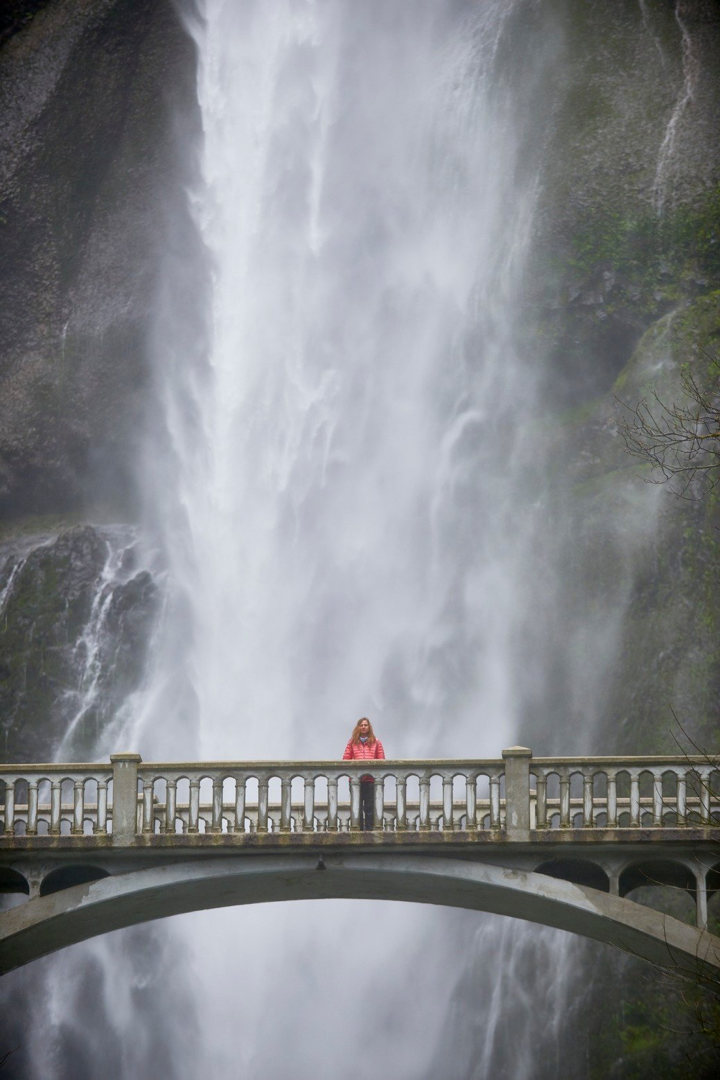 person standing on bridge in front of huge waterfall