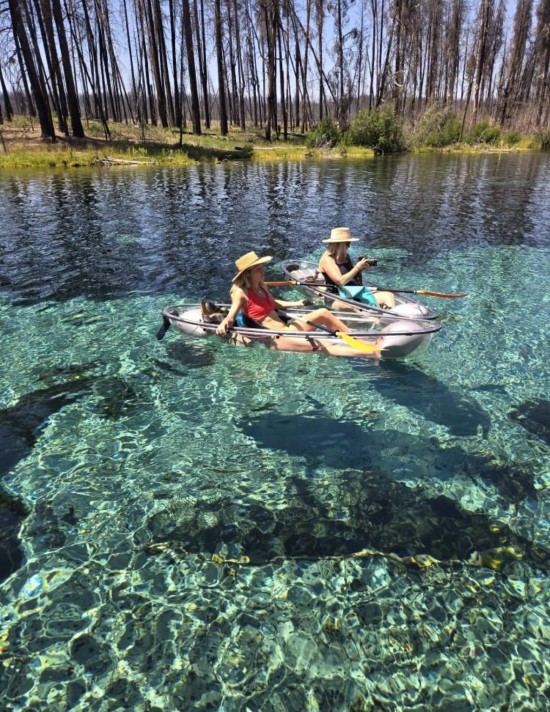people in clear bottom kayaks smiling while floating on clear blue water
