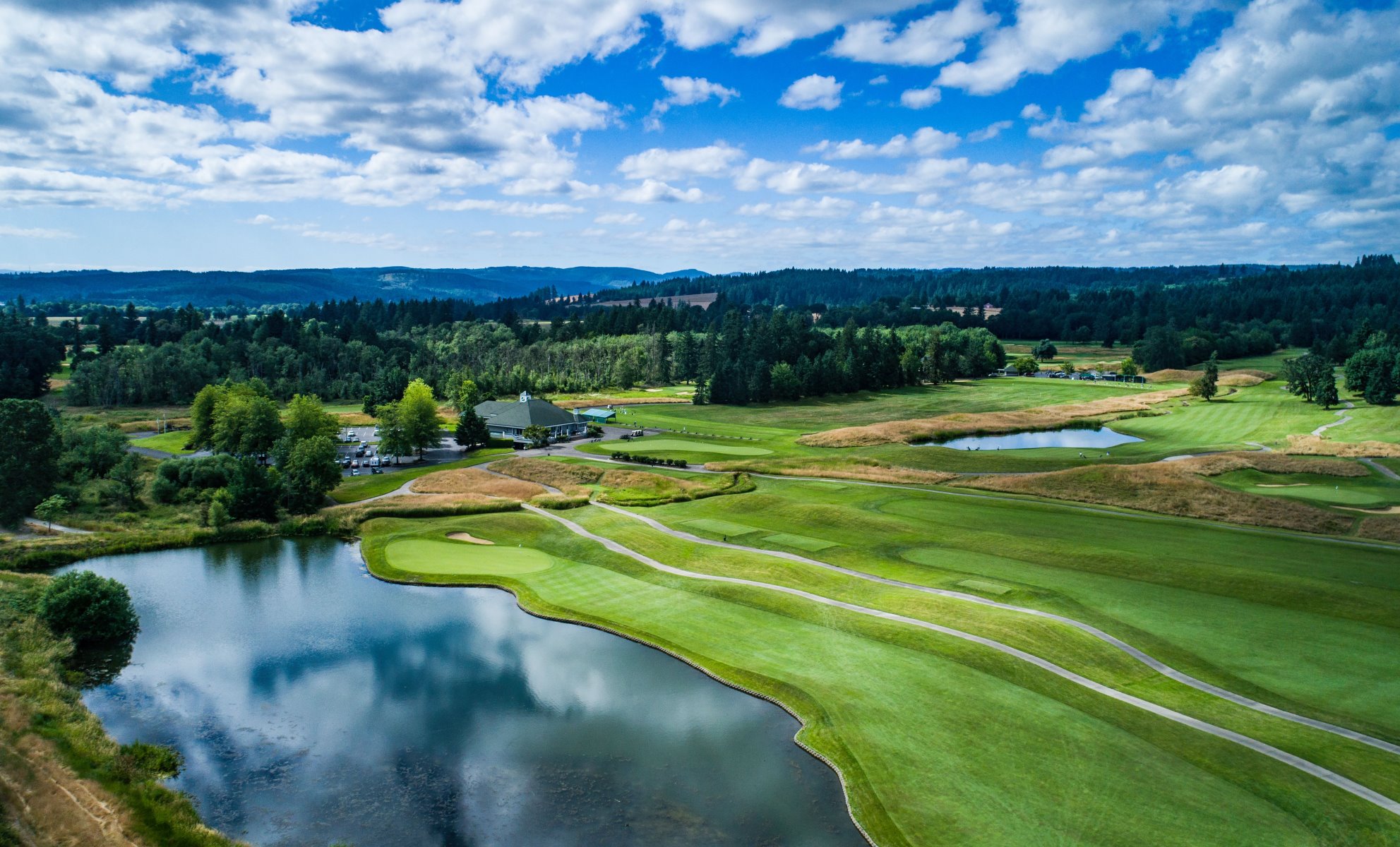 aerial view of golf course with water feature and blue skies with white clouds