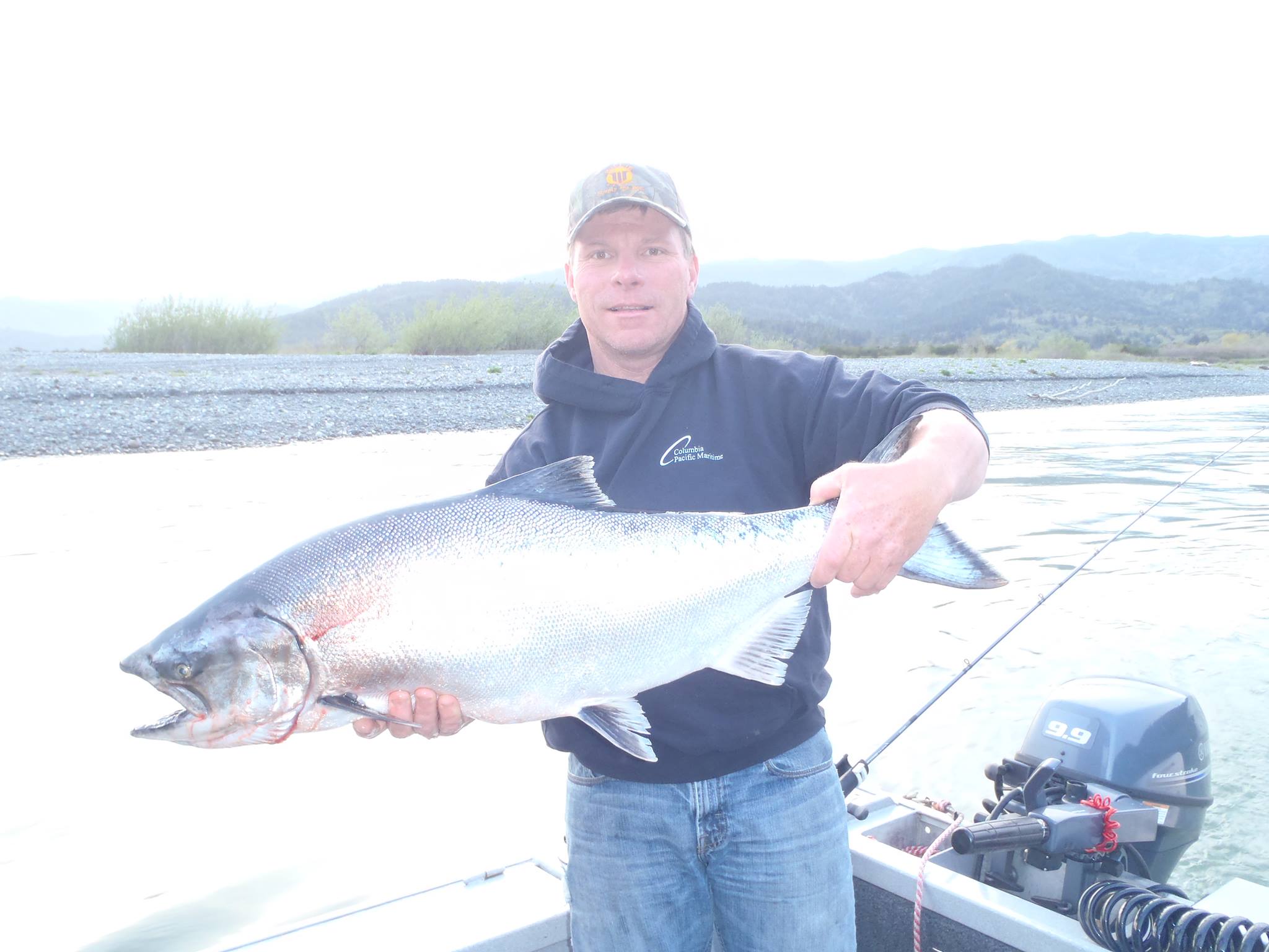 man stands in boat holding large fish he just caught