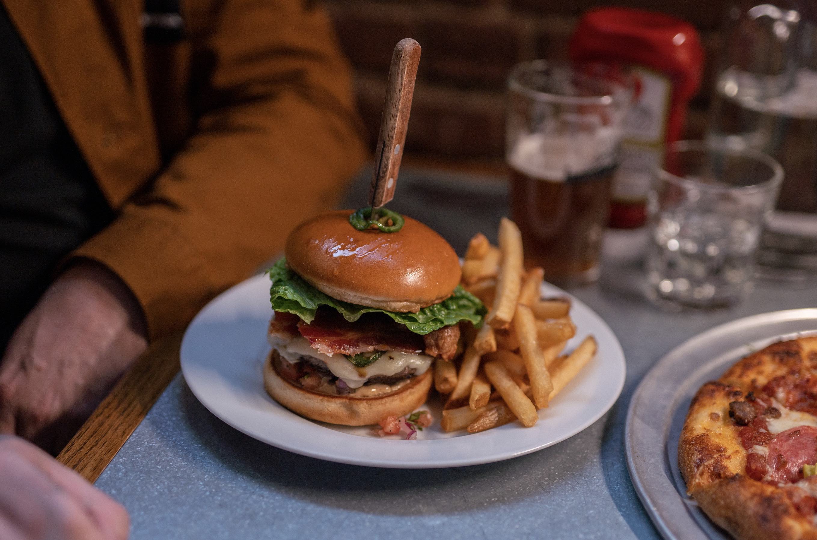 There is a large burger and fries, stacked with ingredients and a knife through the top