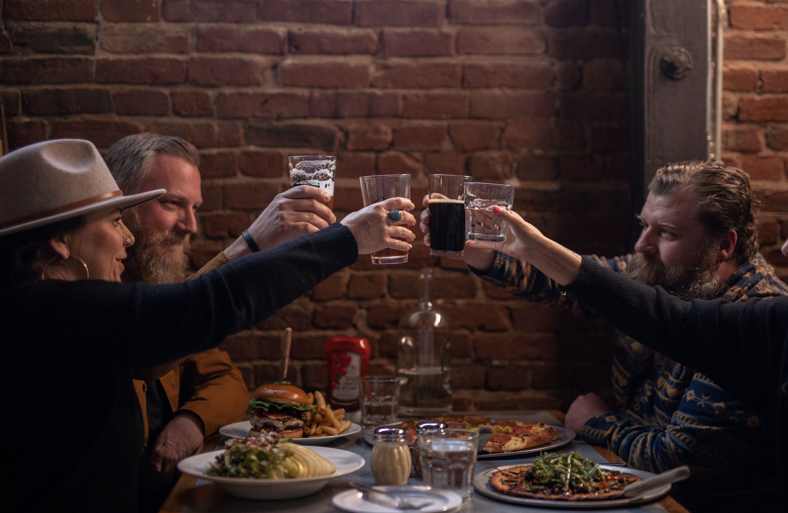 People cheers above a table full of food in front of a brick wall