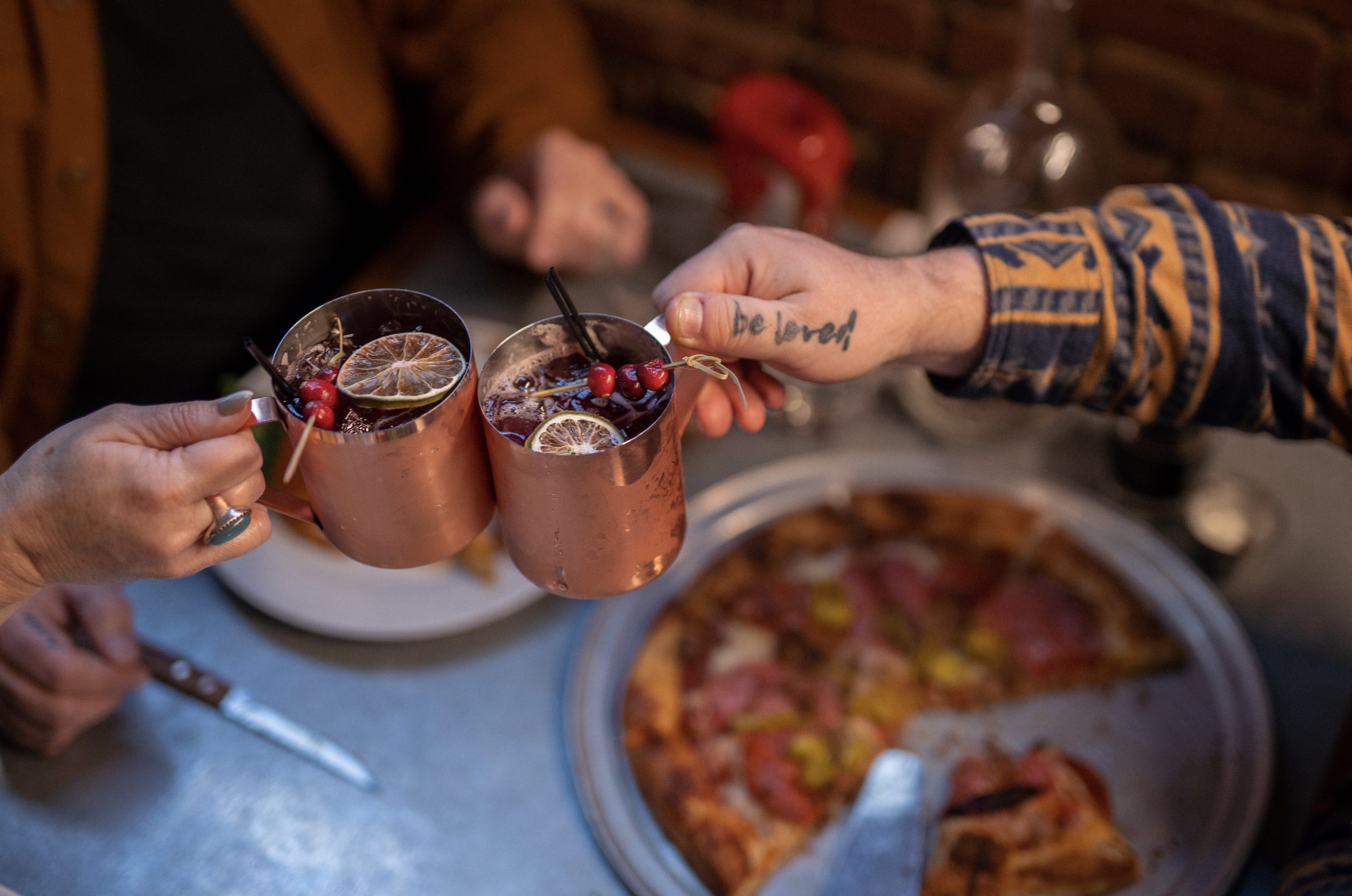 Copper mugs with garnished drinks cheers above a pizza