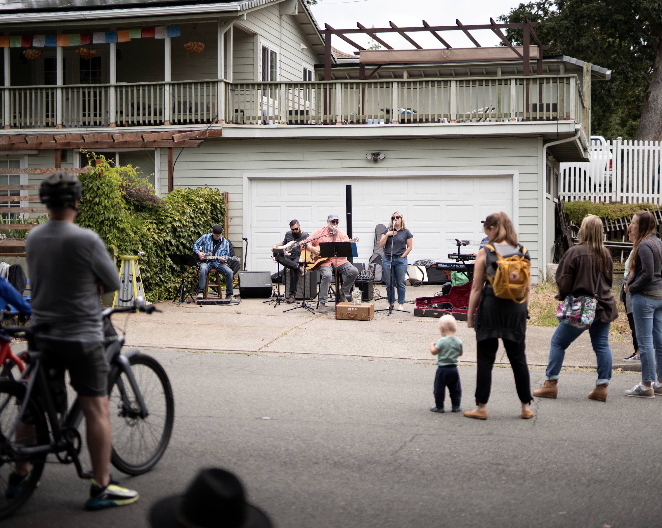 Bikers and pedestrians gathered around a driveway where a band is playing live music
