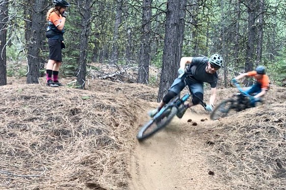 Two riders race on outdoor trail course with instructer observing.