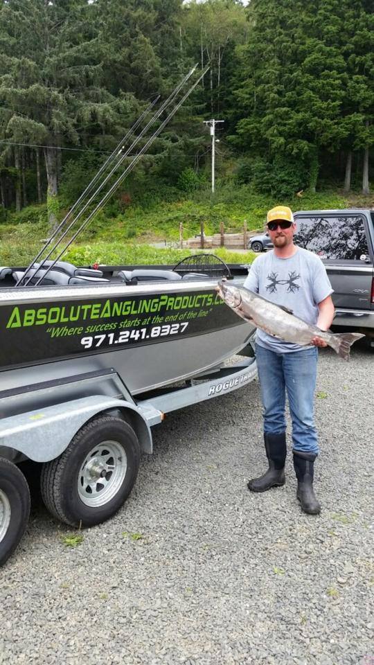 Fisherman standing next to the guide boat which is on a trailer. Fisherman is holding a large salmon.