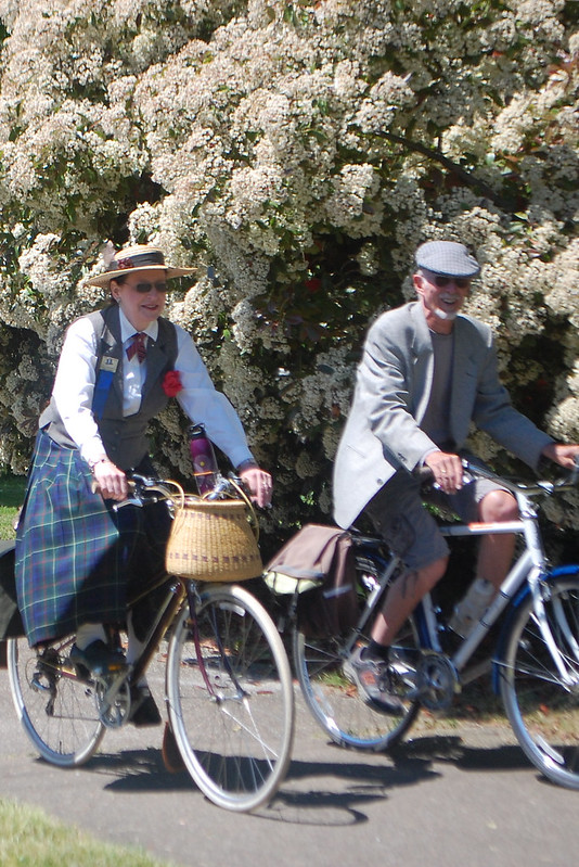 a man and a woman riding bikes in tweed attire