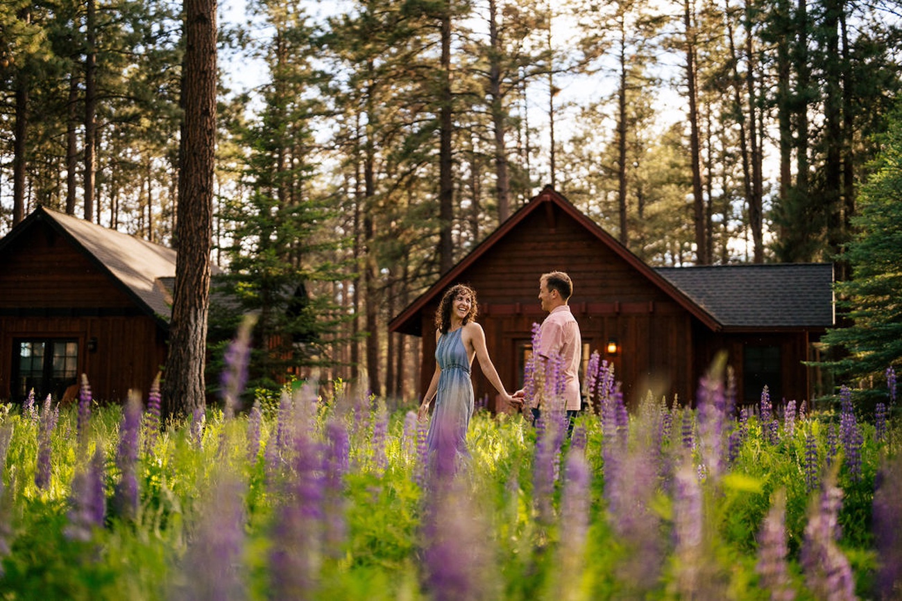 couple wandering through lupine landscape with cabins in the background