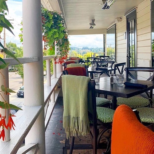 Wooden chairs with green upholstered seats are positioned around wooden tables on Baird's on B's covered patio balcony