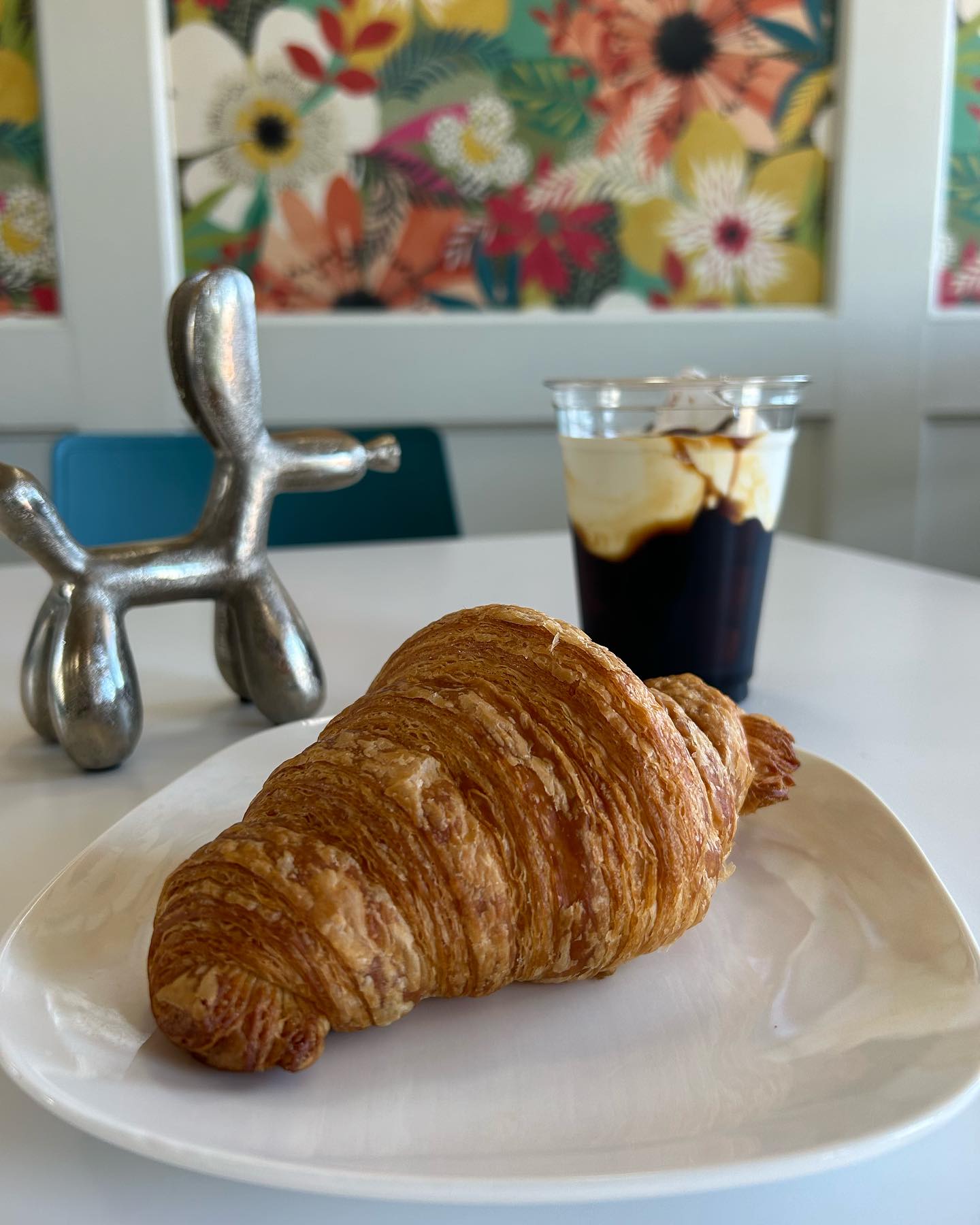Scone and coffee ice cream drink sit on a white table. Floral print wallpaper in the background
