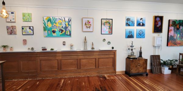 Display wall at imperfecta with hanging art. Against the wall is a long wooden side table with sculptures and artefacts