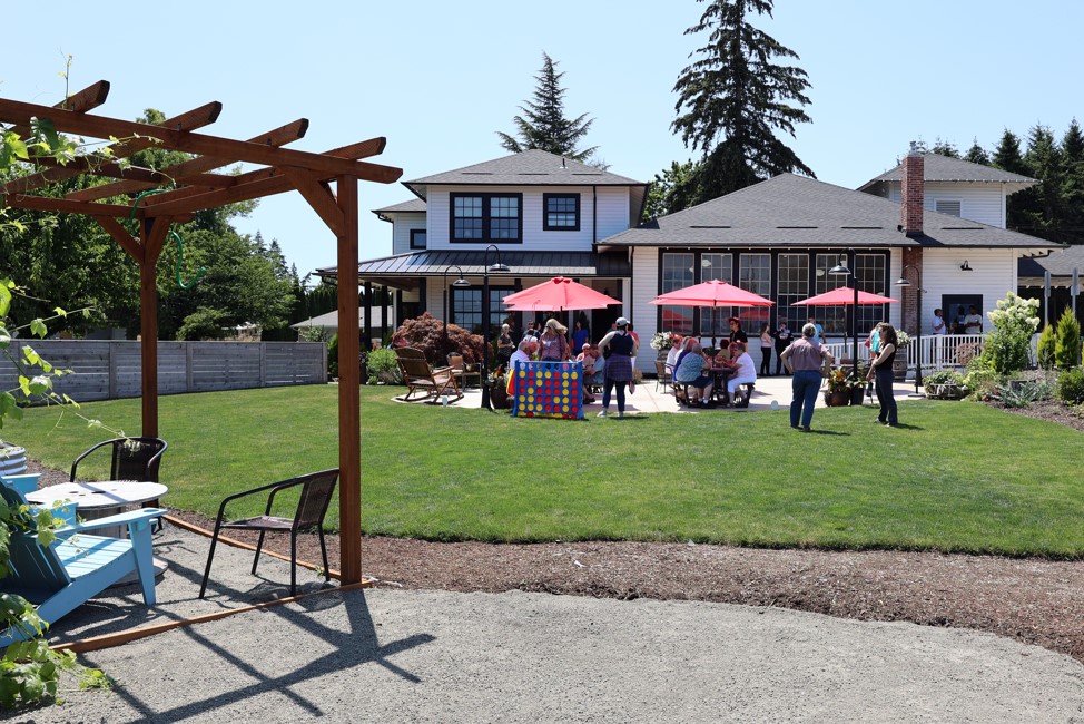 A crowd of people sit at tables under red umbrellas on the patio of Whiskey Hill Store