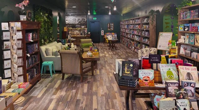 Cozy bookstore interior with wooden shelves filled with books, seating areas, and vibrant displays of local literature and gifts.