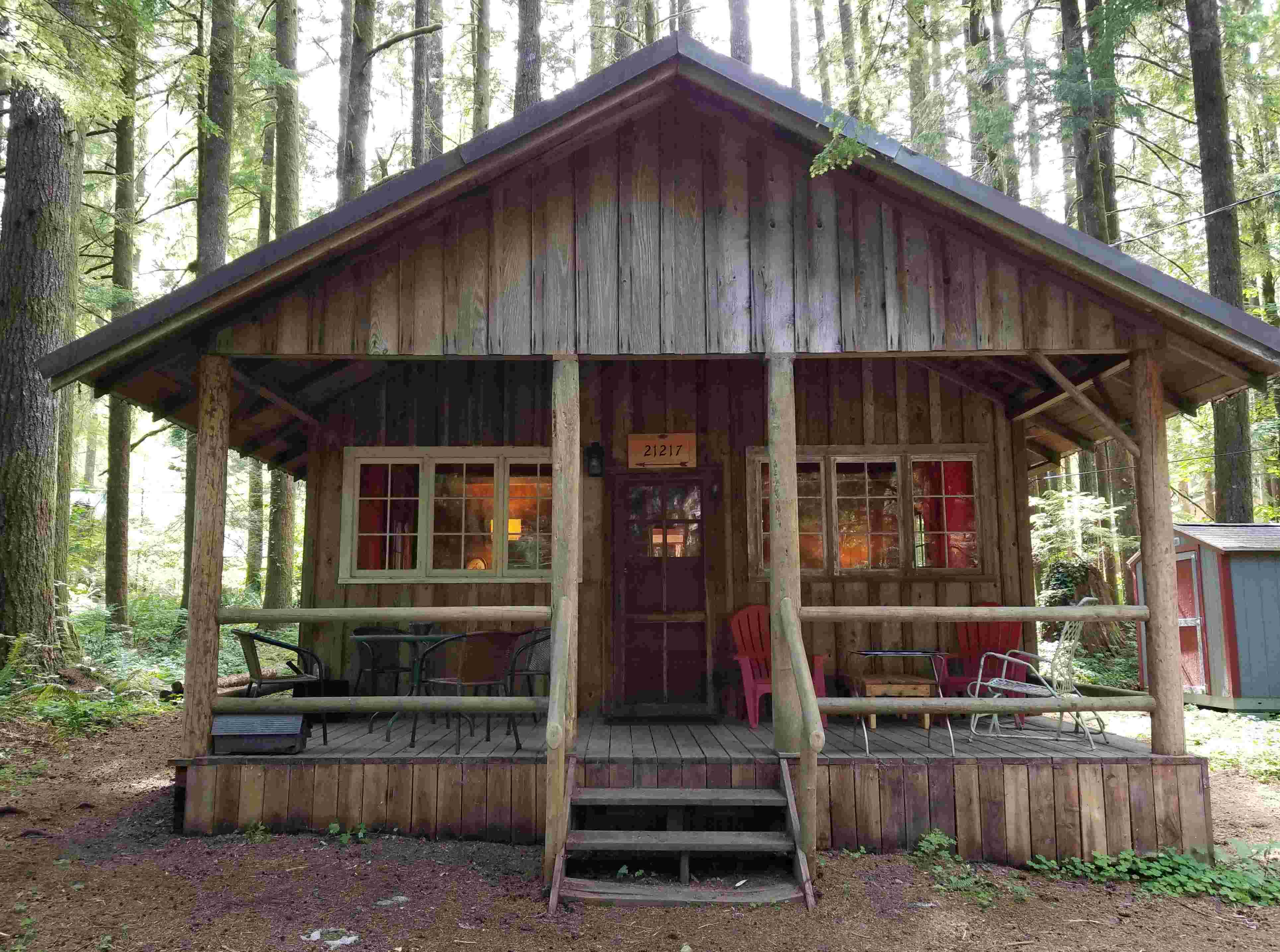 View of the front of a cedar cabin in the woods. Steps lead up to the cabin's large front porch with a gabled patio cover.