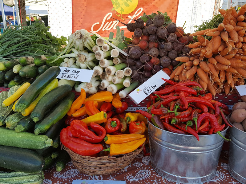 Buckets of zucchini, peppers, beets and carrots at a farmers market table