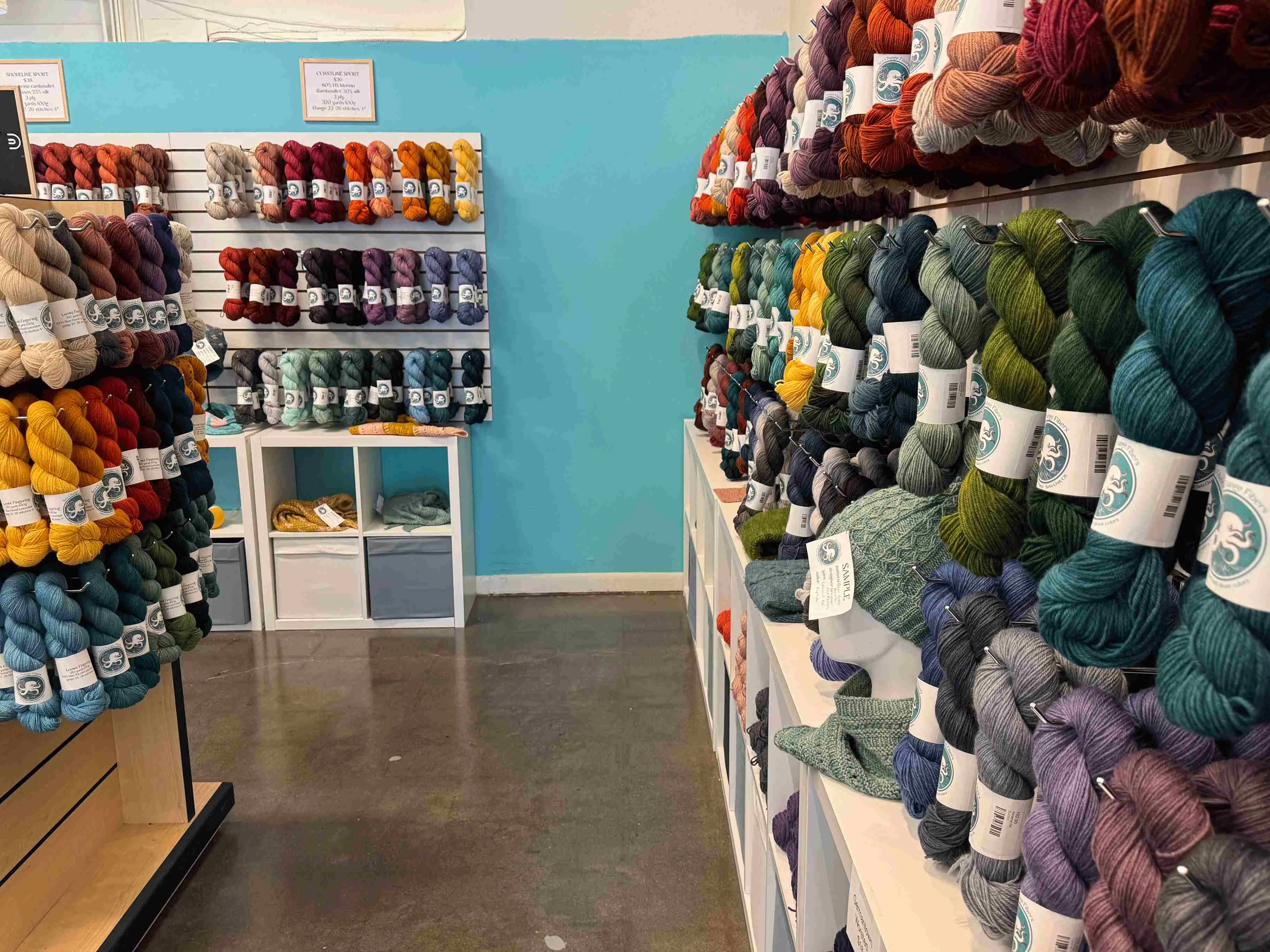 A vibrant yarn shop interior featuring shelves lined with colorful skeins of yarn. Displays showcase various textures and hues.