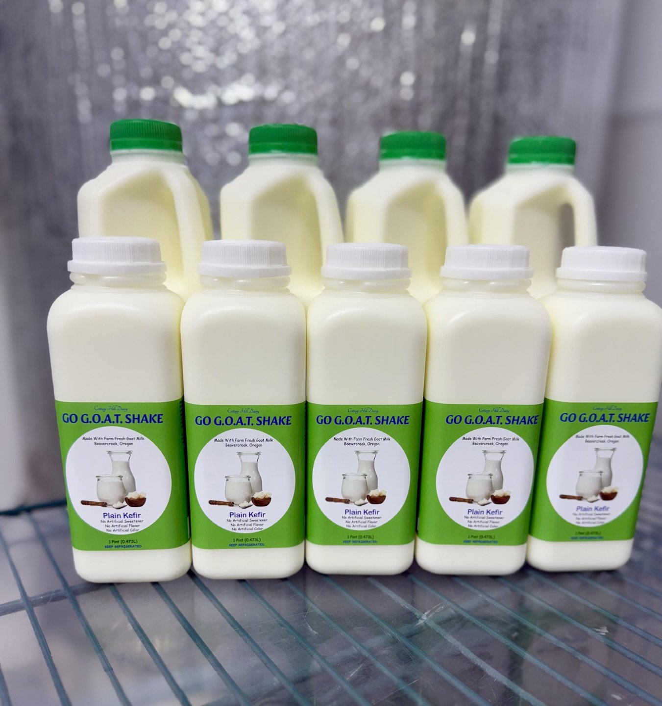 Bottles of "Go G.O.A.T. Shake" lined up on a shelf, featuring a green label with a goat illustration and product details.