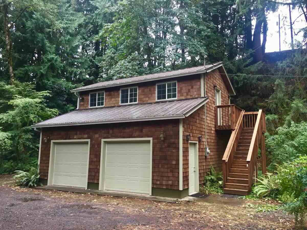 Two story cedar clad house with double garage doors in front and stairs leading to a second level front door.