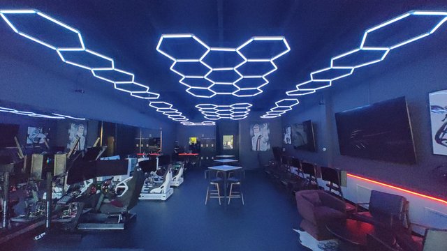A modern gaming lounge featuring hexagonal LED ceiling lights, gaming stations, and sleek furniture, creating a vibrant atmosphere.