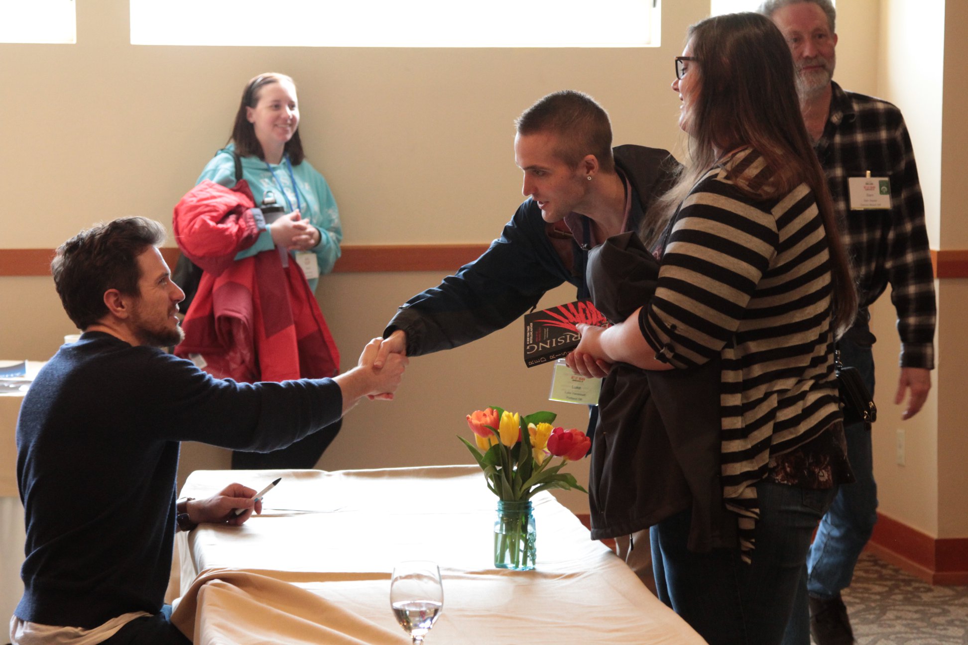A reader shaking an author's hand over a book signing table.