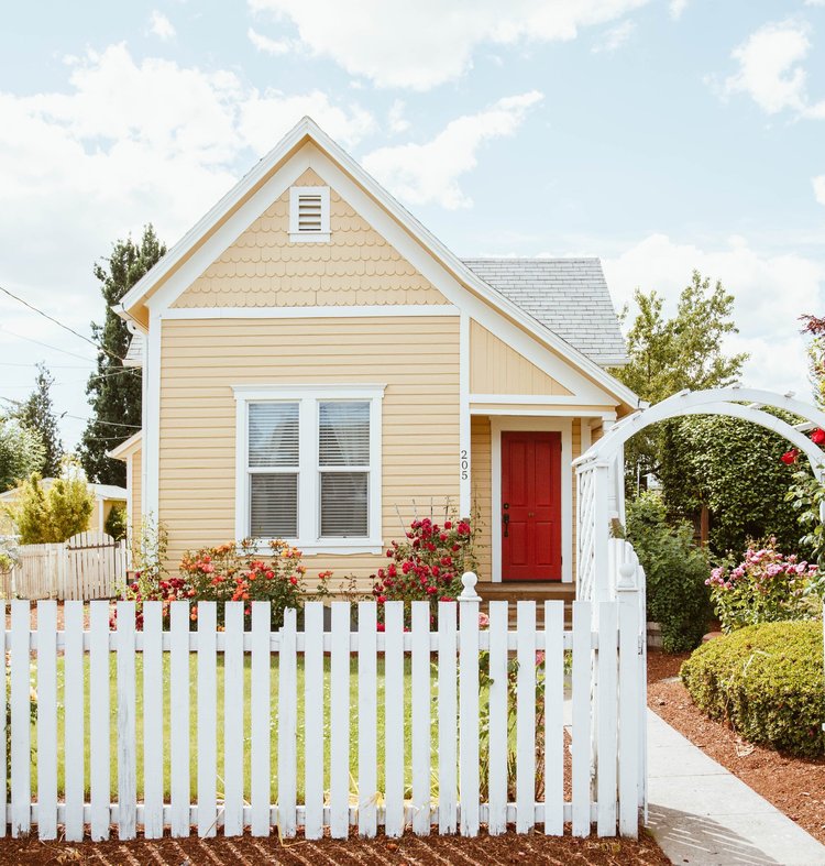 Front of a small home with a white picket fence and white archway