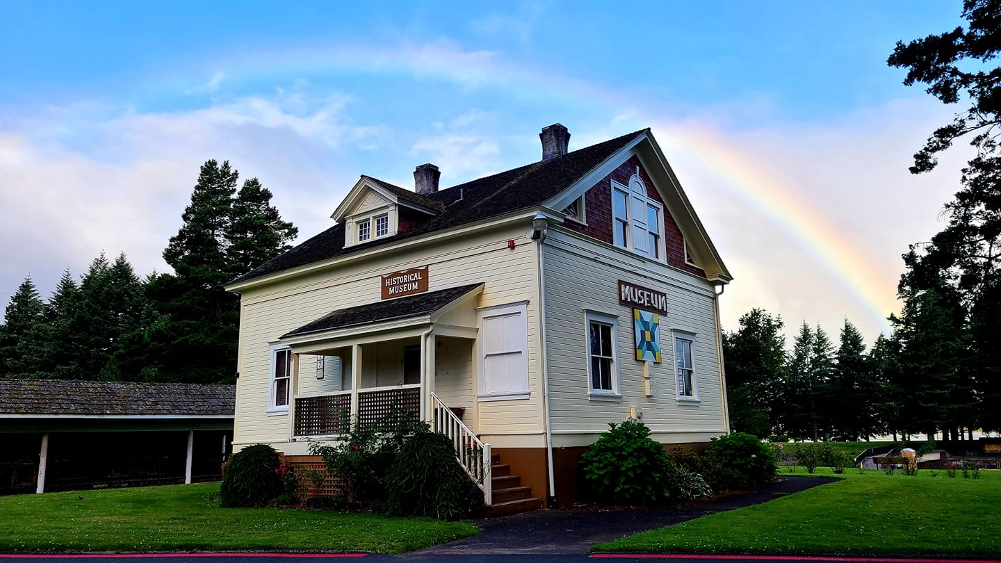 rear entrance of cascade locks historical museum. building has white siding and brown roof with a rainbow in the sky above