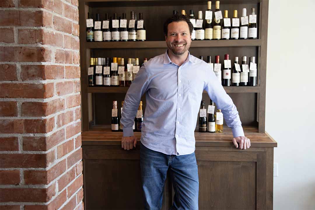 Man posing in front of shelf of wine