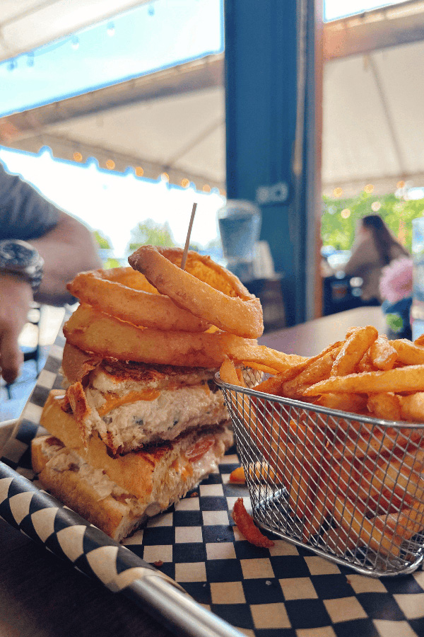 burger topped with onion rings on a tray next to basket of French fries