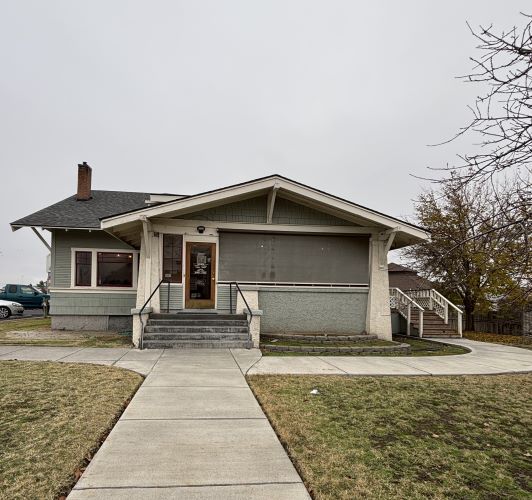 A paved sidewalk leads to a gray-blue house with stairs. It has been converted to a restaurant